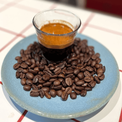 Angelique’s Finest Fair Chain Espresso Blend als Crema zubereitet, dekoriert mit Kaffeebohnen.